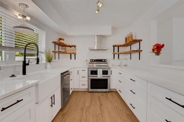 1320 Dixie Ln S, Saint Petersburg, FL 33707 - kitchen with open shelves, appliances with stainless steel finishes, wall chimney range hood, light wood-style floors, and white cabinetry