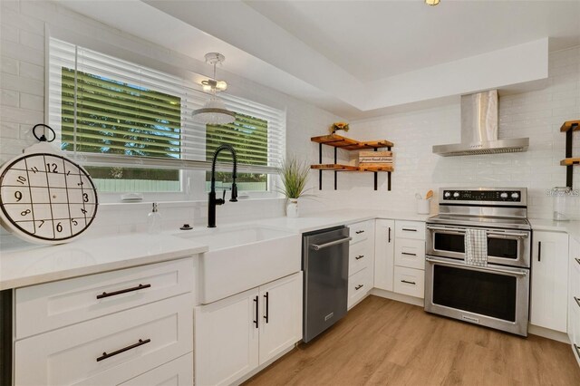 1320 Dixie Ln S, Saint Petersburg, FL 33707 - kitchen featuring stainless steel appliances, wall chimney exhaust hood, open shelves, white cabinetry, and light wood-type flooring