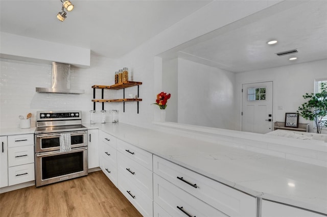 1320 Dixie Ln S, Saint Petersburg, FL 33707 - kitchen with range with two ovens, wall chimney exhaust hood, white cabinetry, light wood-type flooring, and light stone counters