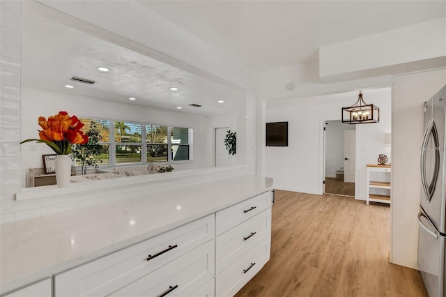1320 Dixie Ln S, Saint Petersburg, FL 33707 - kitchen with light wood-style floors, white cabinetry, freestanding refrigerator, light stone countertops, and a chandelier