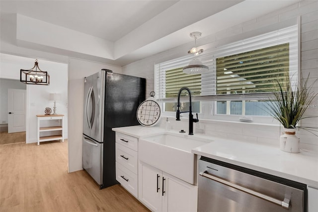 1320 Dixie Ln S, Saint Petersburg, FL 33707 - kitchen with stainless steel appliances, white cabinetry, pendant lighting, light wood-type flooring, and a chandelier
