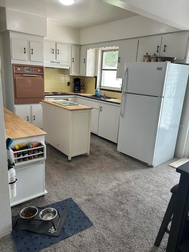 4917 99th St N, Saint Petersburg, FL 33708 - kitchen featuring freestanding refrigerator, wall oven, under cabinet range hood, decorative backsplash, and white cabinets