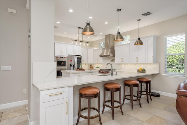 3042 Wentworth Way, Tarpon Springs, FL 34688 - kitchen featuring wall chimney range hood, appliances with stainless steel finishes, a peninsula, decorative backsplash, and white cabinetry