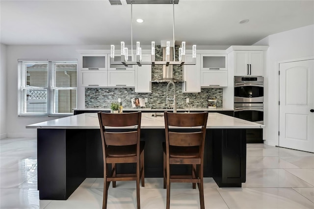 3241 Evening Breeze Loop, Wesley Chapel, FL 33544 - kitchen featuring double oven, decorative backsplash, an island with sink, glass insert cabinets, and recessed lighting