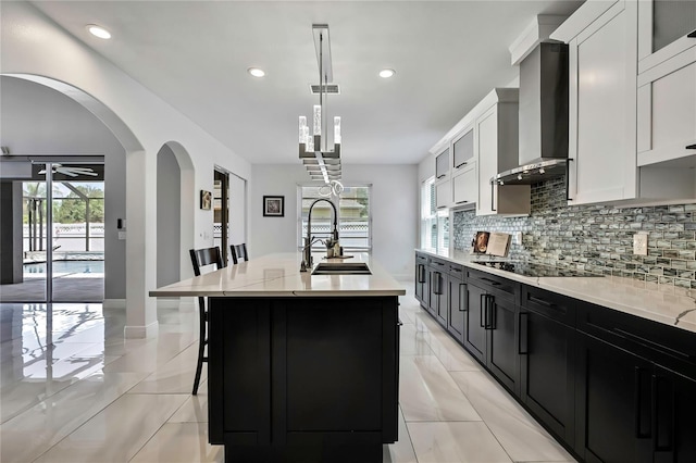 3241 Evening Breeze Loop, Wesley Chapel, FL 33544 - kitchen with wall chimney exhaust hood, tasteful backsplash, an island with sink, black electric stovetop, and dark cabinetry