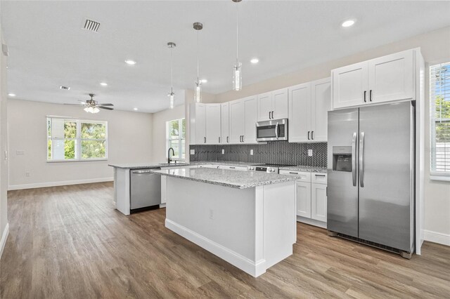 8319 N Ogontz Ave, Tampa, FL 33604 - kitchen featuring stainless steel appliances, wood finished floors, a kitchen island, backsplash, and white cabinetry