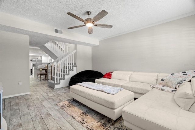 3323 Fox Hunt Dr, Palm Harbor, FL 34683 - living room featuring ceiling fan, stairs, a textured ceiling, light wood finished floors, and crown molding