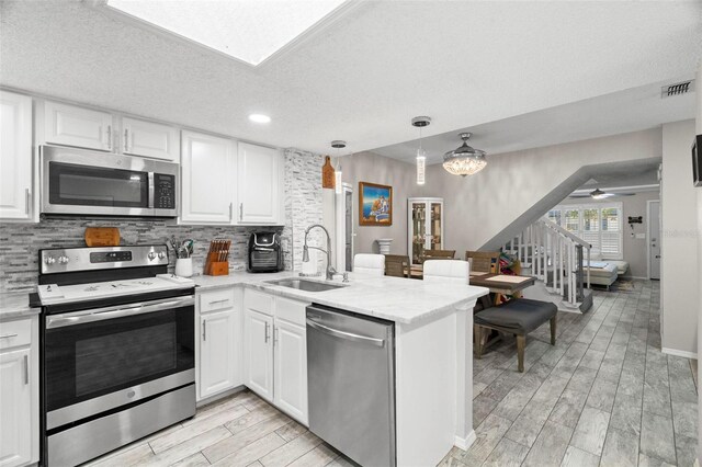 3323 Fox Hunt Dr, Palm Harbor, FL 34683 - kitchen featuring stainless steel appliances, tasteful backsplash, a peninsula, light wood finished floors, and white cabinets