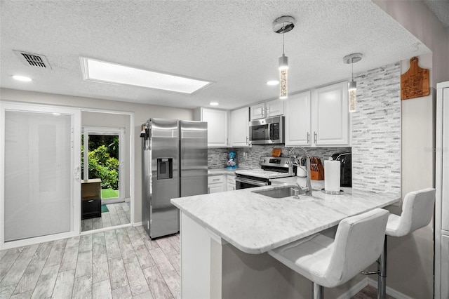 3323 Fox Hunt Dr, Palm Harbor, FL 34683 - kitchen with appliances with stainless steel finishes, a peninsula, tasteful backsplash, a textured ceiling, and light wood-type flooring