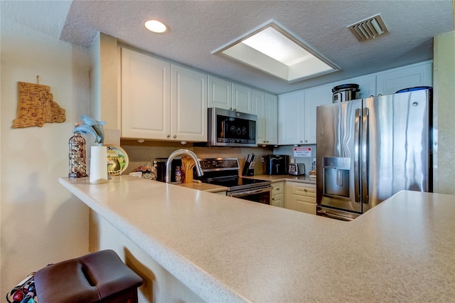 163 Brent Cir, Oldsmar, FL 34677 - kitchen featuring appliances with stainless steel finishes, a textured ceiling, a kitchen breakfast bar, light countertops, and white cabinets