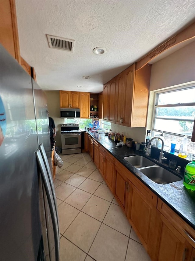 kitchen featuring stainless steel appliances, brown cabinets, a textured ceiling, light tile patterned floors, and open shelves