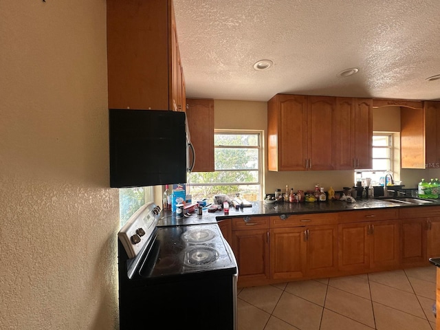 kitchen with black range with electric stovetop, a textured ceiling, brown cabinetry, plenty of natural light, and dark countertops