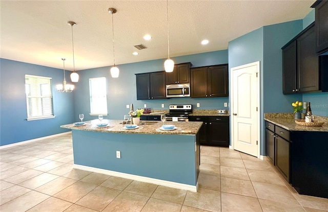 10621 Scenic Hollow Dr, Riverview, FL 33578 - kitchen with appliances with stainless steel finishes, light stone counters, a textured ceiling, light tile patterned floors, and an island with sink