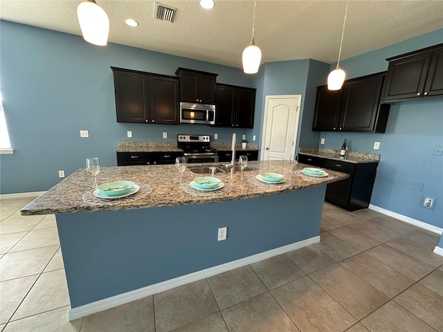 10621 Scenic Hollow Dr, Riverview, FL 33578 - kitchen featuring stainless steel appliances, stone countertops, light tile patterned floors, a textured ceiling, and a center island with sink