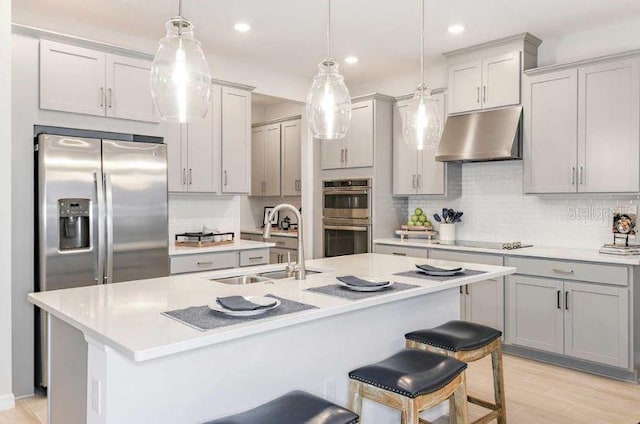 33618 Castaway Loop, Wesley Chapel, FL 33543 - kitchen with appliances with stainless steel finishes, under cabinet range hood, a center island with sink, recessed lighting, and gray cabinetry