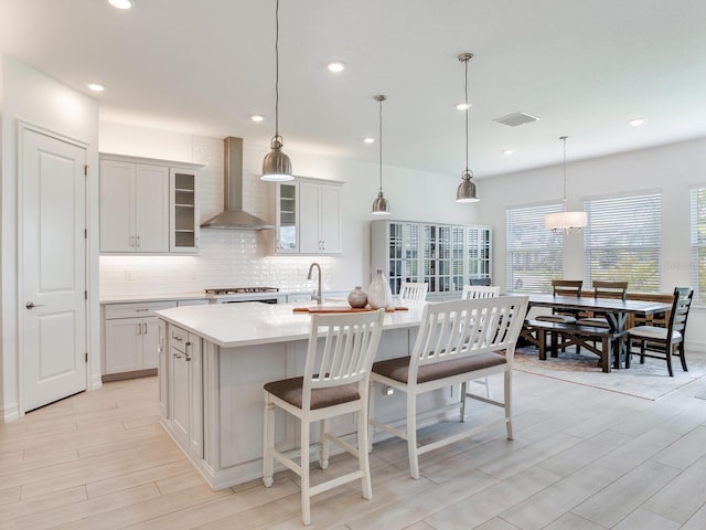 6057 Marsh Trail Dr, Odessa, FL 33556 - kitchen with wall chimney range hood, decorative backsplash, light countertops, a kitchen island with sink, and light wood-style floors