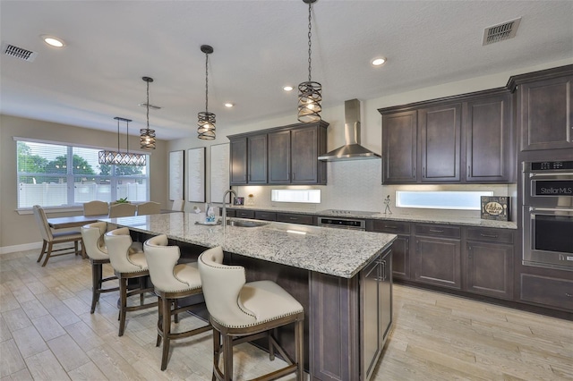 2866 Quail Crest Ct, Valrico, FL 33594 - kitchen with wall chimney range hood, light wood finished floors, stainless steel double oven, light stone countertops, and recessed lighting