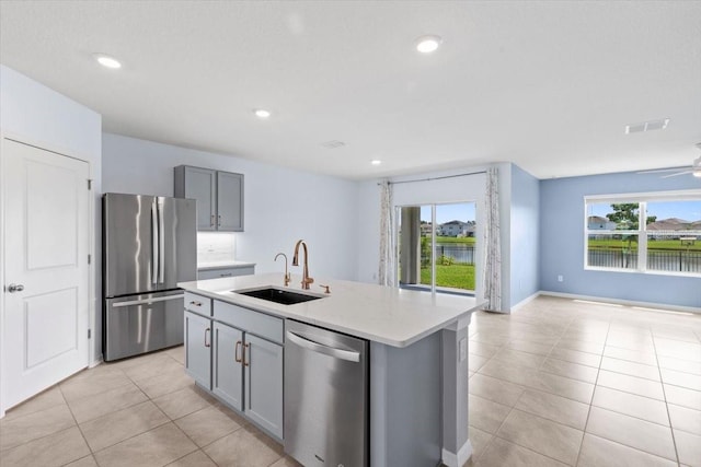 33369 Hamilton Hill Ln, Wesley Chapel, FL 33545 - kitchen featuring appliances with stainless steel finishes, gray cabinetry, light tile patterned floors, open floor plan, and a center island with sink