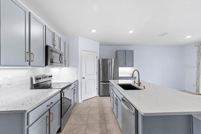 33369 Hamilton Hill Ln, Wesley Chapel, FL 33545 - kitchen featuring stainless steel appliances, gray cabinets, a kitchen island with sink, tasteful backsplash, and light stone countertops