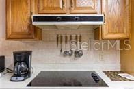 5781 S Utopia Ter, Inverness, FL 34452 - kitchen with under cabinet range hood, light countertops, tasteful backsplash, and brown cabinetry