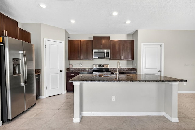 13324 Willow Bluestar Loop, Riverview, FL 33579 - kitchen with appliances with stainless steel finishes, dark stone countertops, light tile patterned floors, a center island with sink, and dark brown cabinetry