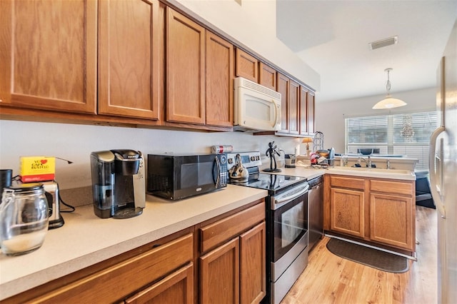 7046 Frascati Loop, Wesley Chapel, FL 33544 - kitchen with appliances with stainless steel finishes, light countertops, a peninsula, brown cabinetry, and light wood-style flooring