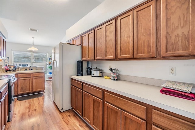 7046 Frascati Loop, Wesley Chapel, FL 33544 - kitchen featuring freestanding refrigerator, brown cabinets, light wood finished floors, and light countertops
