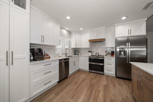 11763 Saree Ct, Largo, FL 33778 - kitchen featuring stainless steel appliances, light countertops, decorative backsplash, white cabinets, and light wood-style flooring