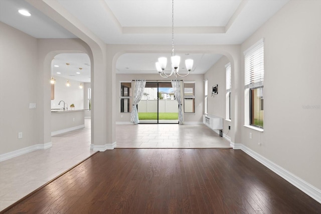 3994 Medicci Ln, Wesley Chapel, FL 33543 - unfurnished dining area featuring a chandelier, wood-type flooring, a raised ceiling, and arched walkways
