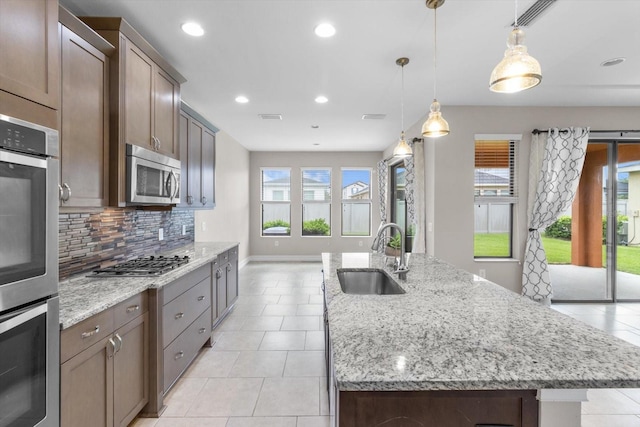 3994 Medicci Ln, Wesley Chapel, FL 33543 - kitchen with stainless steel appliances, tasteful backsplash, an island with sink, light tile patterned flooring, and light stone countertops
