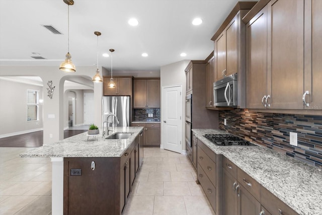 3994 Medicci Ln, Wesley Chapel, FL 33543 - kitchen featuring stainless steel appliances, decorative backsplash, light tile patterned flooring, arched walkways, and light stone countertops
