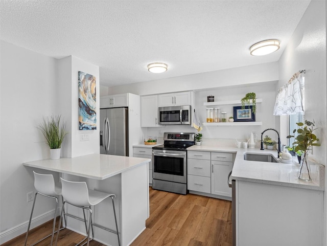 1675 E Grovehill Rd, Palm Harbor, FL 34683 - kitchen with appliances with stainless steel finishes, open shelves, light wood-style floors, a textured ceiling, and light countertops