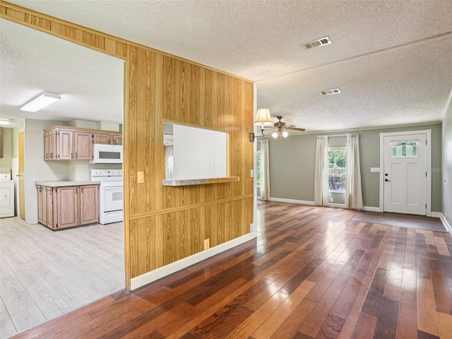 26223 Chianina Dr, Wesley Chapel, FL 33544 - unfurnished living room featuring a textured ceiling, light wood finished floors, ceiling fan, wooden walls, and washer / clothes dryer