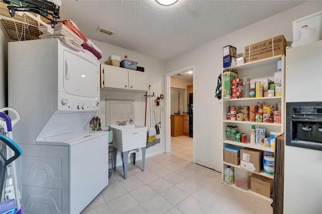1502 Fort Duquesna Dr, Sun City Center, FL 33573 - laundry room with stacked washer / dryer, a textured ceiling, cabinet space, and light tile patterned flooring