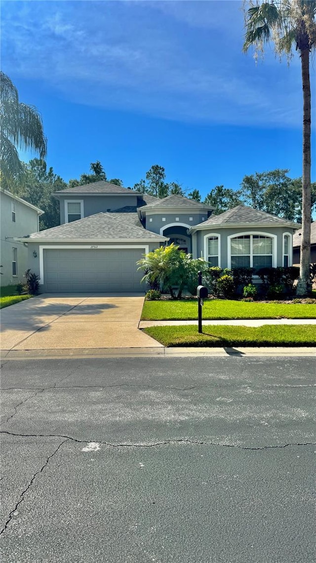 27312 Edenfield Dr, Wesley Chapel, FL 33544 - view of front of house with an attached garage, driveway, stucco siding, a front lawn, and a shingled roof