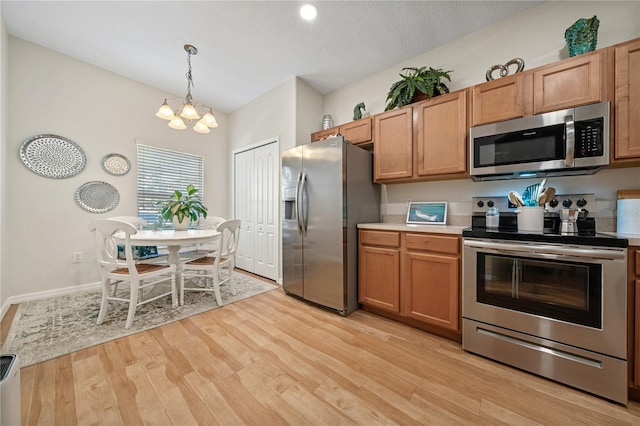 2349 Willimette Dr, Wesley Chapel, FL 33543 - kitchen featuring stainless steel appliances, a chandelier, light countertops, light wood-style floors, and hanging light fixtures