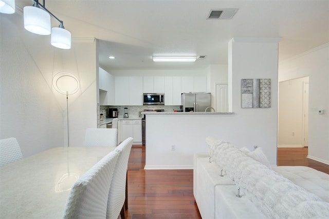 4221 W Spruce St Unit 2328, Tampa, FL 33607 - kitchen featuring stainless steel appliances, dark wood finished floors, white cabinets, decorative backsplash, and crown molding
