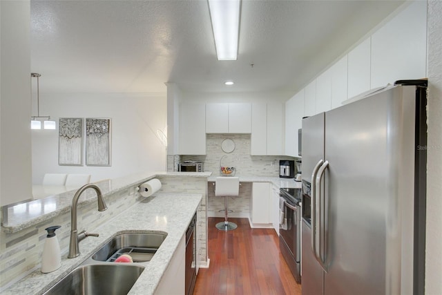 4221 W Spruce St Unit 2328, Tampa, FL 33607 - kitchen with appliances with stainless steel finishes, decorative backsplash, white cabinets, decorative light fixtures, and dark wood-style flooring
