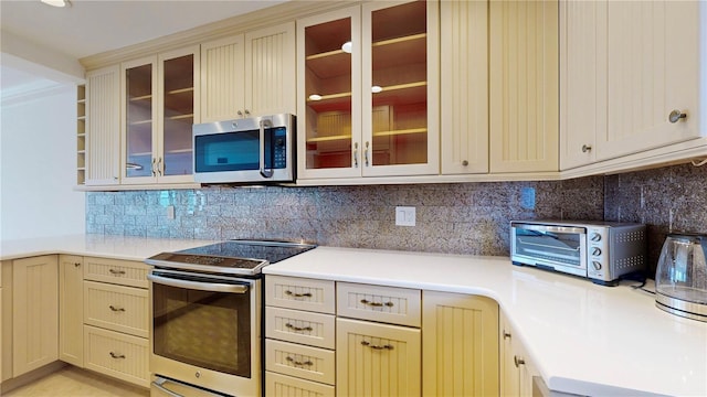 4950 Gulf Blvd Unit 903, St Pete Beach, FL 33706 - kitchen featuring appliances with stainless steel finishes, light countertops, tasteful backsplash, glass insert cabinets, and cream cabinets