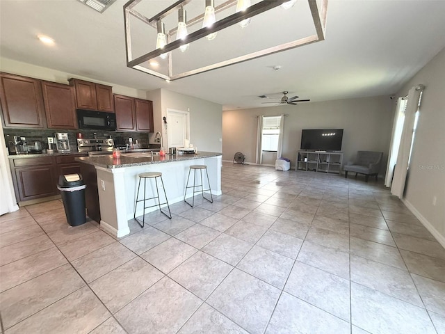 10221 Carloway Hills Dr, Wimauma, FL 33598 - kitchen featuring black microwave, stainless steel range with electric cooktop, tasteful backsplash, a kitchen island with sink, and light tile patterned floors