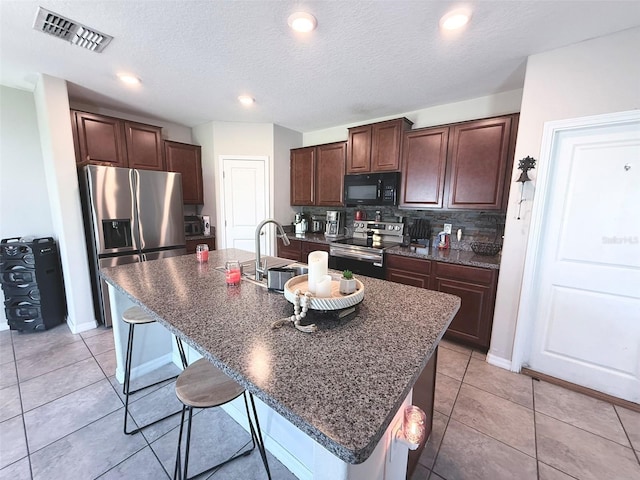 10221 Carloway Hills Dr, Wimauma, FL 33598 - kitchen featuring appliances with stainless steel finishes, a breakfast bar area, an island with sink, decorative backsplash, and dark brown cabinetry
