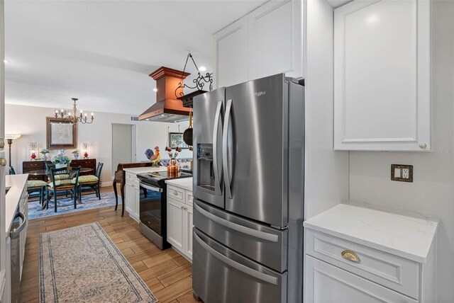 621 77th Ave, St Pete Beach, FL 33706 - kitchen with stainless steel appliances, white cabinets, light wood finished floors, island exhaust hood, and a chandelier