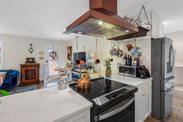 621 77th Ave, St Pete Beach, FL 33706 - kitchen with island range hood, stainless steel appliances, light wood-style floors, and white cabinetry
