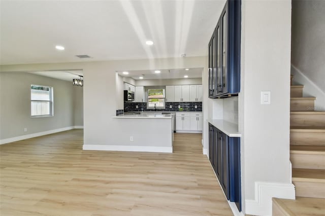 7806 N Matanzas Ave, Tampa, FL 33614 - kitchen featuring stainless steel microwave, light wood-style floors, tasteful backsplash, white cabinetry, and open floor plan