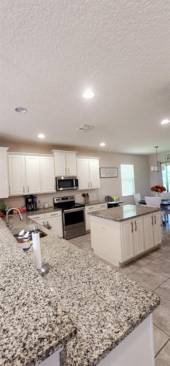 1704 Felicity Ln, Kissimmee, FL 34744 - kitchen with stainless steel appliances, a kitchen island, a textured ceiling, white cabinetry, and light stone counters