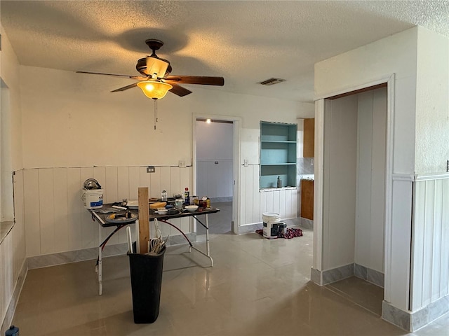 6711 Arroyo Dr, New Port Richey, FL 34652 - dining room featuring a textured ceiling, ceiling fan, and a wainscoted wall
