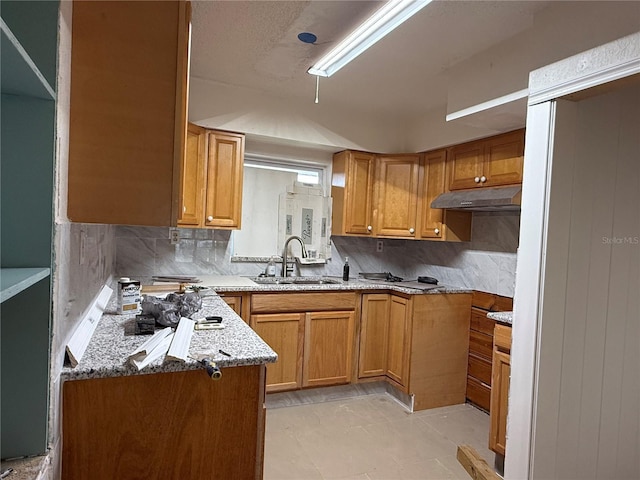 6711 Arroyo Dr, New Port Richey, FL 34652 - kitchen featuring under cabinet range hood, backsplash, light stone counters, and brown cabinets