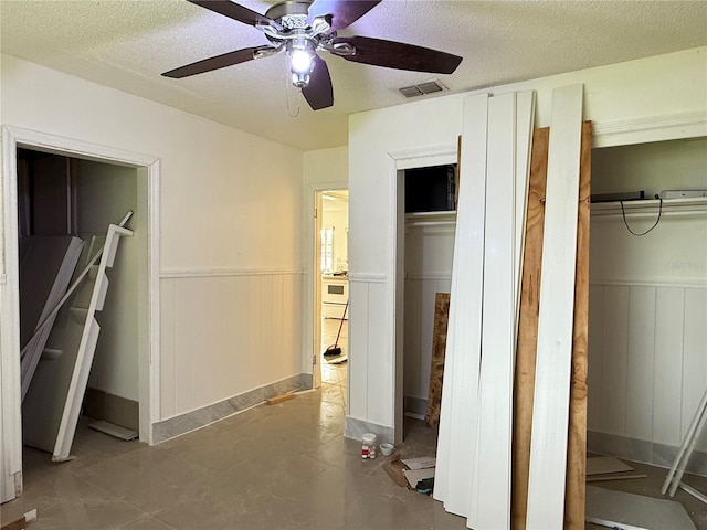 6711 Arroyo Dr, New Port Richey, FL 34652 - unfurnished bedroom featuring a wainscoted wall, a textured ceiling, two closets, and ceiling fan