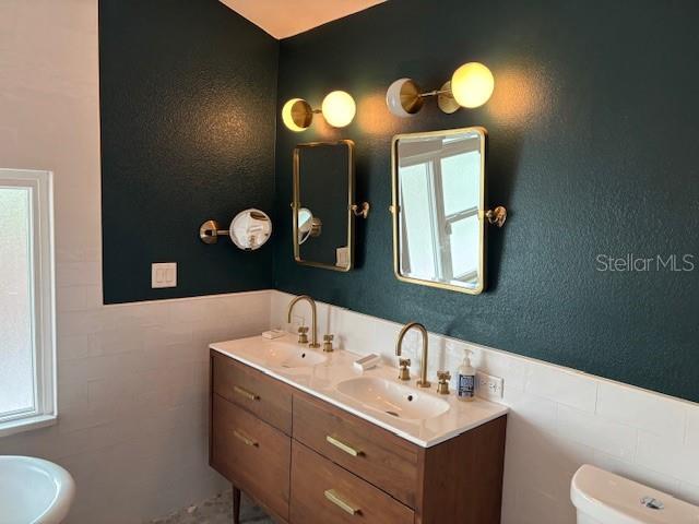 1601 14th St N, Saint Petersburg, FL 33704 - bathroom with tile walls, double vanity, plenty of natural light, and a wainscoted wall