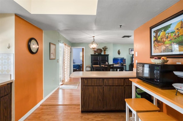 9171 Horizon Dr, Spring Hill, FL 34608 - kitchen featuring black microwave, light wood finished floors, light countertops, a peninsula, and a chandelier